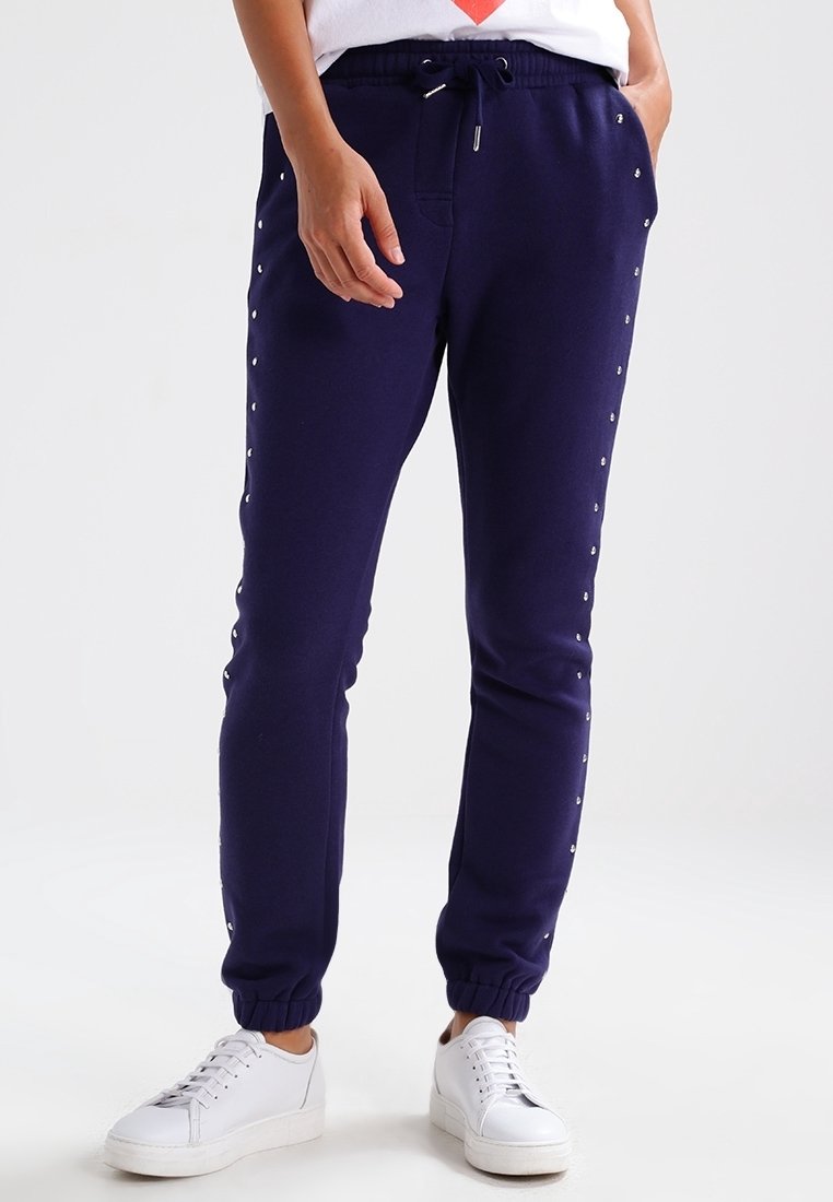 Navy blue sweatpants with elastic cuffs, featuring silver studded detailing along the sides and a drawstring waist for adjustable fit.