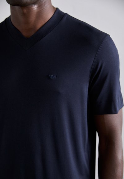 Navy blue v-neck t-shirt made of smooth fabric, featuring short sleeves and a small logo on the left chest. Subtle texture throughout.