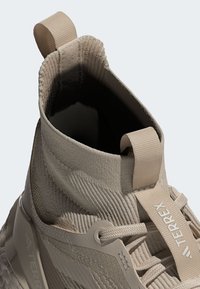 Kremo spalvos aukštos sportinės bateliai su tekstūruota medžiaga viršuje, su rankena, sustiprinta padu, su raištelių sistema ir prekės ženklu.