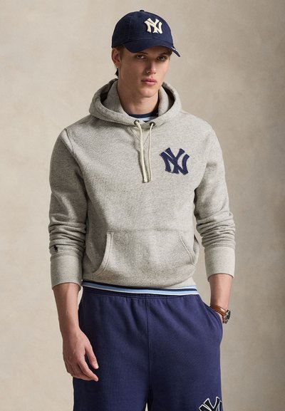 Siva bombažna jopa s prednjim žepom in mornarsko modrim logotipom New York Yankees. Kombinirana z mornarsko modrimi trenirkami z belim in modrim robom.