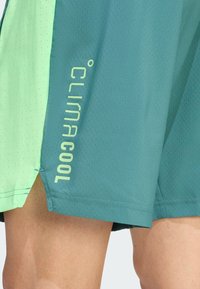 Teal en lichtgroene sportshorts met een textuurstof en een mesh-patroon, en het 'CLIMACOOL' logo in geel-groen op de zijkant gedrukt.