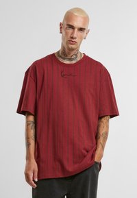 Rød oversized t-shirt med sorte lodrette striber, rund hals, korte ærmer og subtilt logo på brystet. Lavet af blødt stof.