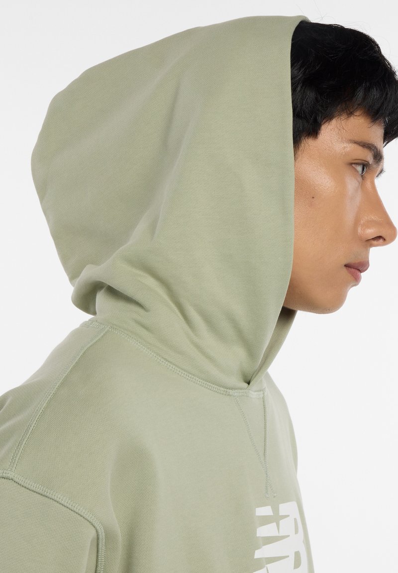 Sweat à capuche vert clair avec cordon de serrage. Texture lisse, détails de couture visibles, et graphique blanc imprimé sur le devant.