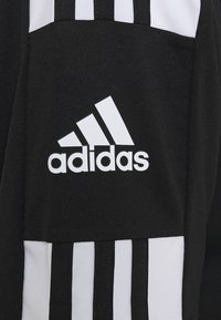 Svart idrottstopp med vita vertikala randdetaljer och en vit Adidas-logga. Materialet verkar slätt med en mjuk textur.