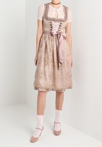 Traditionelles Dirndl mit einem beigen Mieder mit filigraner Flechtung, einem rosa Blumenrock und einem dazu passenden Satinband. Accessoires umfassen Spitzenstrümpfe.