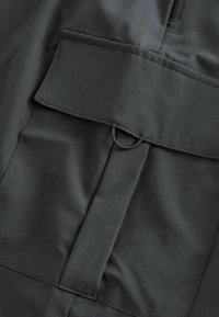 Zwarte stof met een gladde textuur heeft een voorflapzak en een lusdetail, wat een minimalistisch ontwerp en functionele elementen toont.