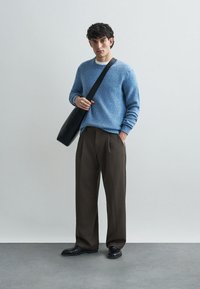 Pull en maille bleu clair, pantalon marron taille haute et chaussures noires. Un sac à bandoulière noir est porté en travers du corps. Design simple et moderne.