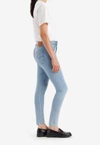 Vaqueros skinny azul claro con dobladillo deshilachado, hechos de denim. Cuenta con dos bolsillos traseros y un parche de cuero marrón en la cintura. Se combina con zapatos negros.