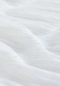 White fabric with soft, textured waves, featuring thin, vertical pleats that create a flowing appearance. Lightweight and sheer material.