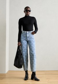 Black long-sleeve top, light blue patterned high-waisted jeans, black heeled boots, and a black pleated tote bag. Sunglasses complete the look.