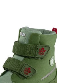 Stivali invernali verdi per bambini con cinturini in Velcro, parte superiore in tessuto testurizzato e logo rosso a contrasto. Design impermeabile con colletto imbottito.