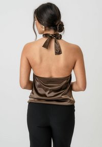 Brązowy satynowy top na ramiączkach z kokardą przy szyi, charakteryzujący się gładką fakturą i odkrytymi plecami, w połączeniu z czarnymi spodniami.