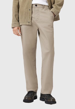 Beige trousers made of smooth fabric, featuring side pockets and a straight fit. Paired with black lace-up shoes for contrast.