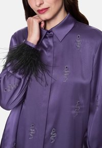 Purple satin blouse with black feather accents on the cuffs, featuring shimmering snake patterns embellished with rhinestones.