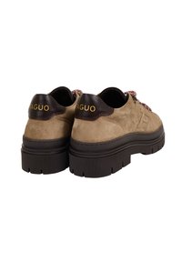 Un paio di scarpe in suede beige con suole spesse di colore marrone scuro, linguette sul tallone marrone scuro con il testo giallo "FAGUO" e lacci pattern, viste da dietro.