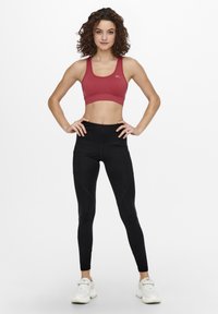 Reggiseno sportivo rosso con un design aderente, abbinato a leggings neri a vita alta con cuciture laterali e scarpe da ginnastica bianche.
