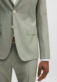 Giacca grigia chiara realizzata in tessuto texturizzato, dotata di chiusura a due bottoni, rever a punta e cuciture a contrasto. Include tasche frontali e una vestibilità slim.