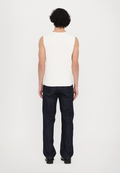 Weiße gestreifte ärmellose Bluse mit rundem Ausschnitt, kombiniert mit dunkelblauen Jeans mit geradem Bein und kontrastierenden Nähten.