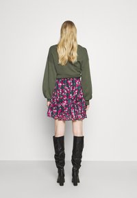 Pull vert oversize, jupe mini rose à motifs floraux, bottes noires montantes, tissu superposé avec volants, texture lisse, taille ajustée.