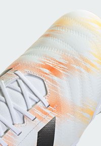 White soccer cleat with orange and yellow gradient patterns, featuring textured material and white laces. Black logo detail on the side.