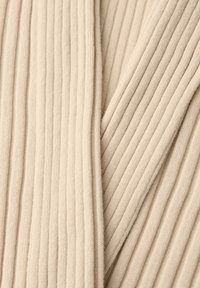 Gros plan d’un tissu tricoté côtelé beige avec des lignes texturées verticales et diagonales qui se chevauchent doucement.