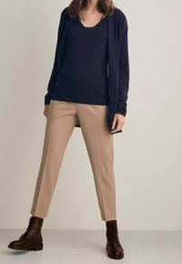 Marineblaues leichtes Langarmoberteil, beiger taillierter Hose und schwarzen Schnürstiefeln, die einen modernen, geschichteten Look mit unterschiedlichen Texturen kreieren.