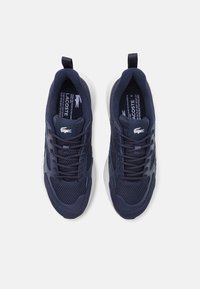 Jūras zila sporta apavi ar sietu un sintētisku materiālu, ar baltu zoli un auklām. Lacoste logo uz sāniem un valkājuma.
