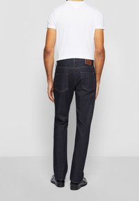 Ciemne dżinsy o prostych nogawkach, z brązową skórzaną naszywką z tyłu na pasku oraz pomarańczowym przeszyciem na kieszeniach.