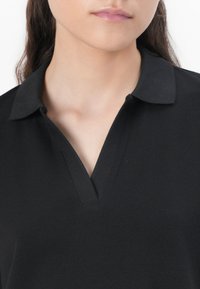 Black polo shirt featuring a structured collar, a deep V-neck design, ribbed texture, and a smooth, durable fabric.