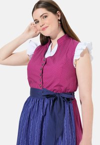 Cuerpo con lunares rosas y cuello alto con botones, mangas rizadas blancas y una falda azul marino con un patrón floral y cintura con lazo.