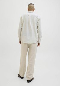 Camisa de manga larga a rayas claras con puños de botón, combinada con pantalones de lino crema. La tela es suave y tiene un ajuste relajado.