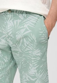 Pantaloni verde chiaro con un motivo di foglie di palma bianche, realizzati in tessuto morbido con una vestibilità comoda e tasche laterali. Chiusura con bottone in vita.