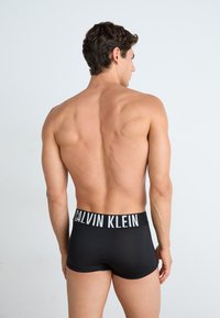 Zwarte boxershorts met een wit Calvin Klein-logo op de tailleband, gladde textuur, aansluitend ontwerp en toont de rug van het model.