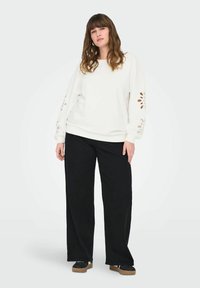 Felpa bianca con ritagli floreali sulle maniche, abbinata a pantaloni larghi neri e scarpe con suola spessa. Design semplice e casual.