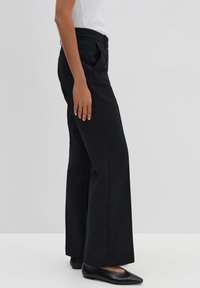 Pantaloni neri a gamba larga realizzati in un tessuto liscio, con tasche laterali e una cintura in vita. Abbinati a scarpe nere a punta flat.