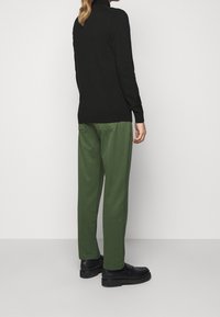 Un pull noir à manches longues avec un col montant associé à un pantalon vert. Le look est complété par des chaussures noires à semelles plates.