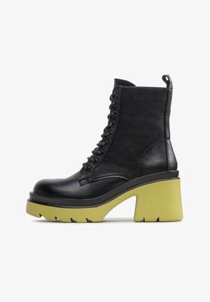 Bota de cuero negro con cordones hasta el tobillo, tacón grueso y amarillo, suela con dibujo de tacos, vista lateral sobre fondo blanco.