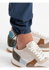 Granatowe dresy z regulowanymi elastycznymi mankietami w połączeniu z beżowymi i brązowymi sneakersami z zamszowymi akcentami i białymi sznurówkami.