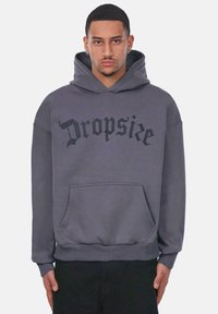 Szary hoodie z przednią kieszenią, na której widnieje napis "Dropsie" w pogrubionej czarnej czcionce. Wykonany z miękkiego materiału, z kapturem na sznurku i ściągaczami na rękawach.