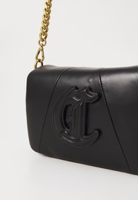 Borsa a mano in pelle nera con logo stilizzato "CL" in rilievo e tracolla in catena dorata con gancio su sfondo bianco semplice.
