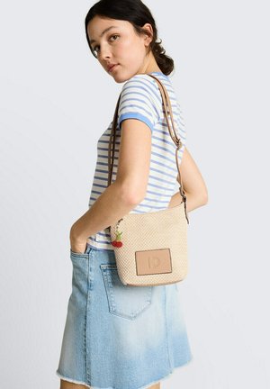 Jonge vrouw met een blauw-wit gestreept T-shirt en een spijkerrok, met een beige gevlochten schoudertas en een kersen-sleutelhanger.