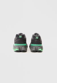 Must must ja hallid New Balance spordijalatsid roheliste aktsentidega vaadatuna tagantpoolt puhta valge tausta ees.