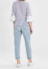 Blusa a righe blu e bianche con maniche a campana bordate in pizzo, vita peplum e schiena a chiave, abbinata a jeans tapered blu chiaro e scarpe bianche.
