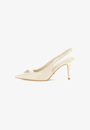 Beige slingback met spits toelopende neus en hoge dunne naaldhak, voorzien van een metallic merklogo detail aan de voorkant.