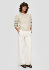 Beige linen blouse with a collared neckline, two front pockets, and elastic cuffs paired with white wide-leg pants featuring side pockets.