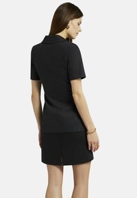 Zwarte jurk met korte mouwen, een kraaghalslijn en een getailleerd silhouet. Glad textuur met een split aan de achterkant. Subtiel verticaal patroon.