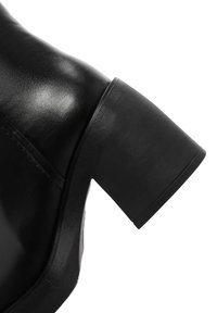 Bottine noire en cuir avec un talon texturé, dotée d'une forme arrondie et d'une finition lisse. Le talon mesure environ deux pouces de hauteur.