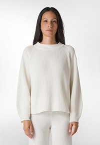 Pulover alb cu dungi, cu guler înalt și umeri căzuți. Textură moale, croială lejeră și design ușor scurt.
