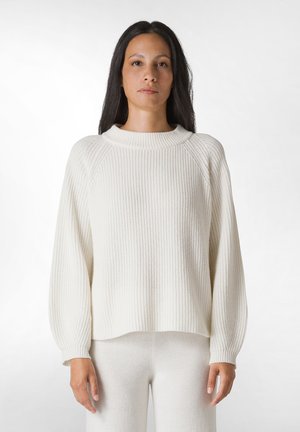 Maglione bianco a costine con colletto alto e spalle scese. Texture morbida, vestibilità ampia e design leggermente accorciato.