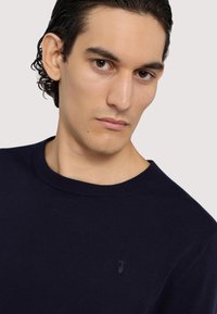 Kaiserblaues Rundhalsausschnitt-Pullover aus weichem Material. Mit einem kleinen, dezenten Logo auf der linken Brust und einem gerippten Kragen.